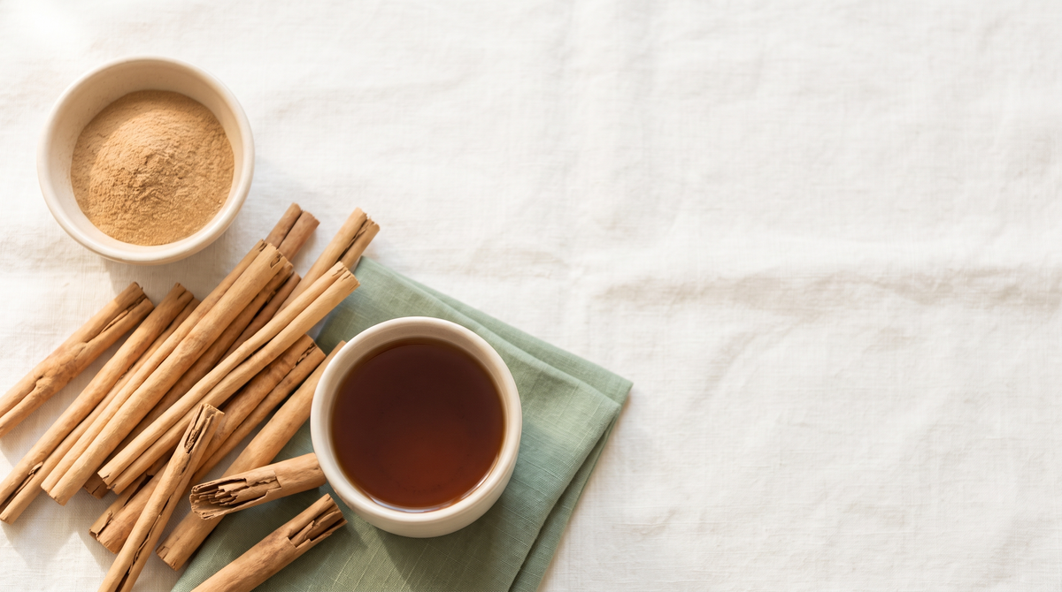 Thin layered Ceylon cinnamon quills, a small bowl of ground cinnamon and a cup of cinnamon tea on cream linen with a sage green napkin.