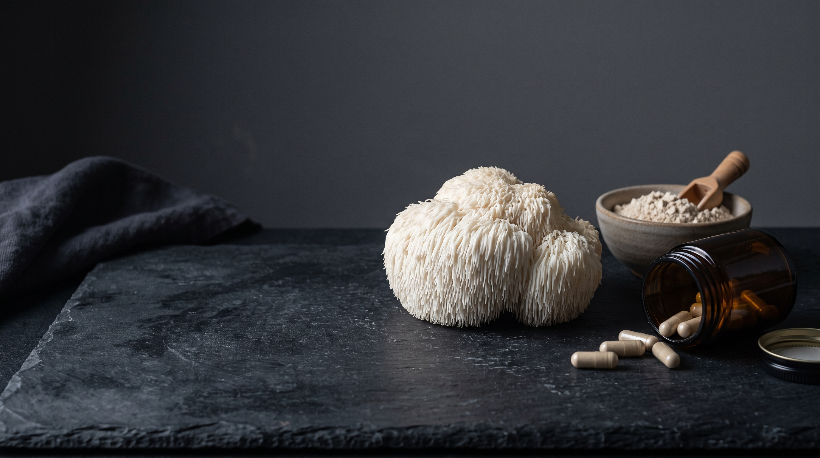 A whole lion's mane mushroom on dark slate beside a bare amber jar of plain capsules and a bowl of pale mushroom powder