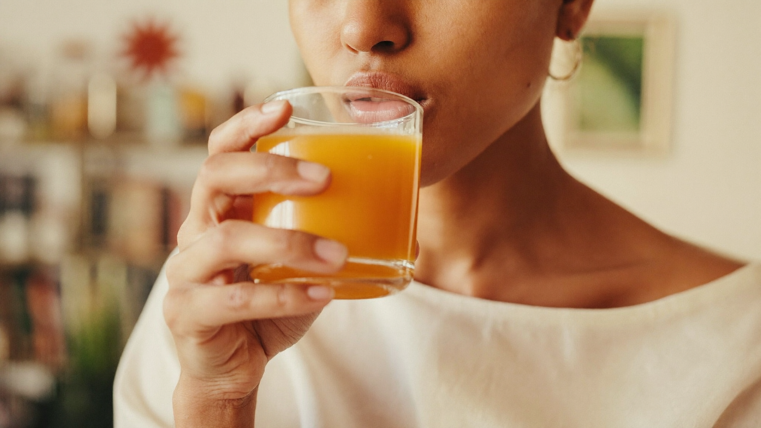 A South Asian woman taking a small golden turmeric and ginger immunity shot in soft morning light.
