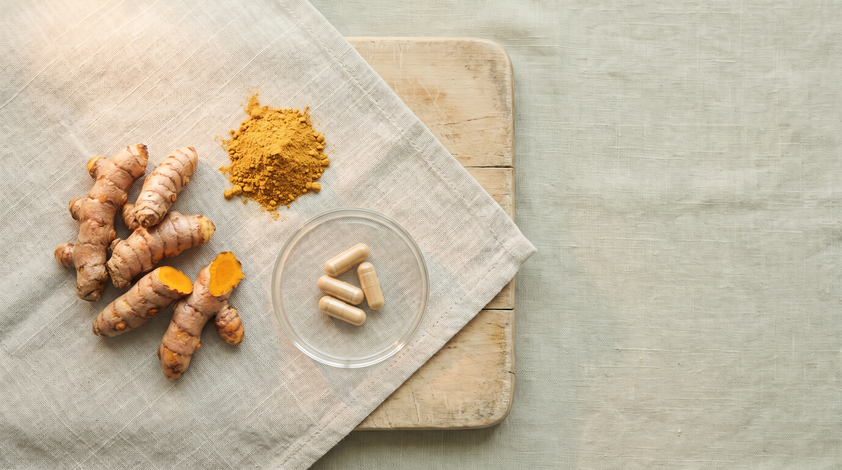 Fresh turmeric rhizomes, a mound of golden turmeric powder and plain capsules in a small glass dish on pale linen