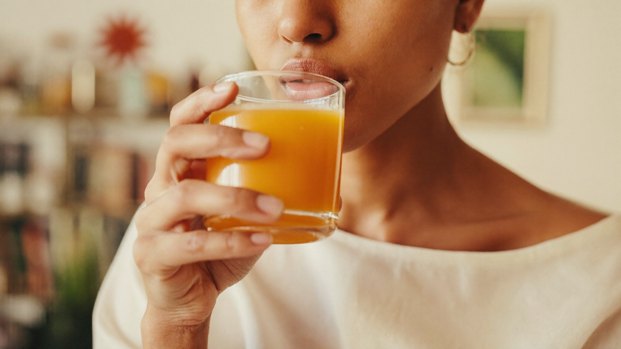 A South Asian woman taking a small golden turmeric and ginger immunity shot in soft morning light.